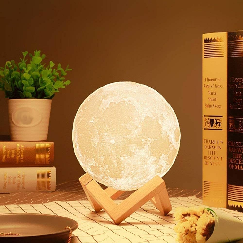 Moon lamp on a wooden stand with books and a plant in the background