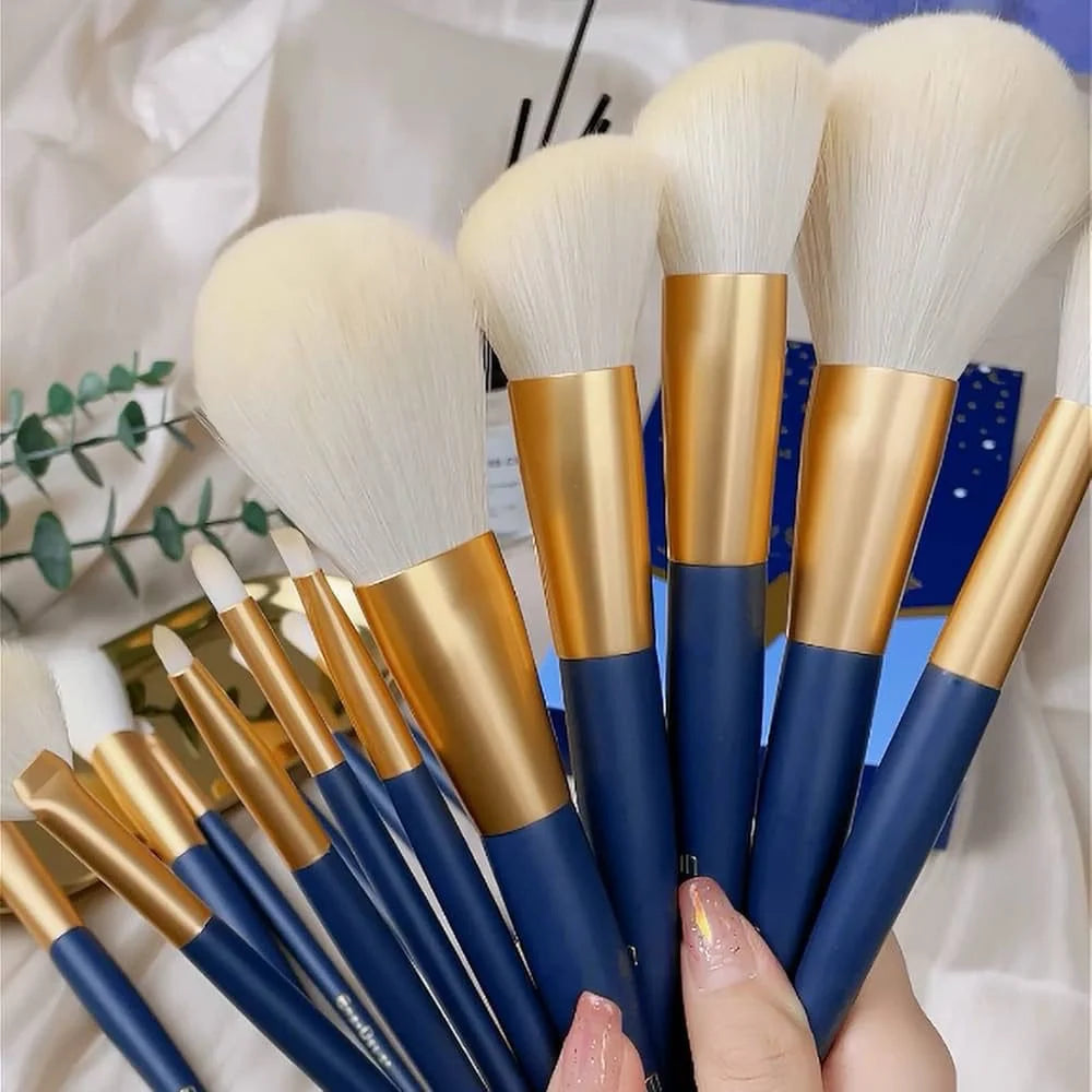 Set of makeup brushes with blue and gold handles held by a hand.