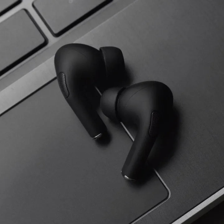 Black wireless earbuds on a dark surface with a laptop