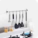 Set of kitchen utensils hanging on a wall-mounted rack above a stove.
