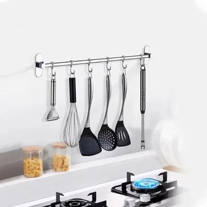 Set of kitchen utensils hanging on a wall-mounted rack above a stove.